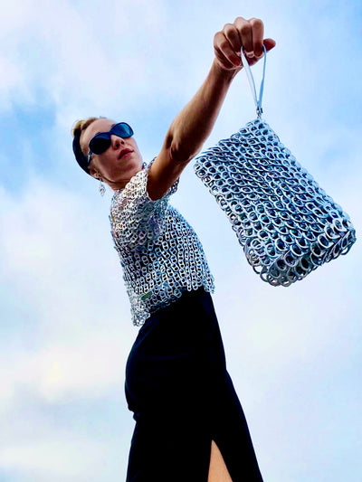 woman holding a metallic silver clutch purse made from soda tabs - escama studio